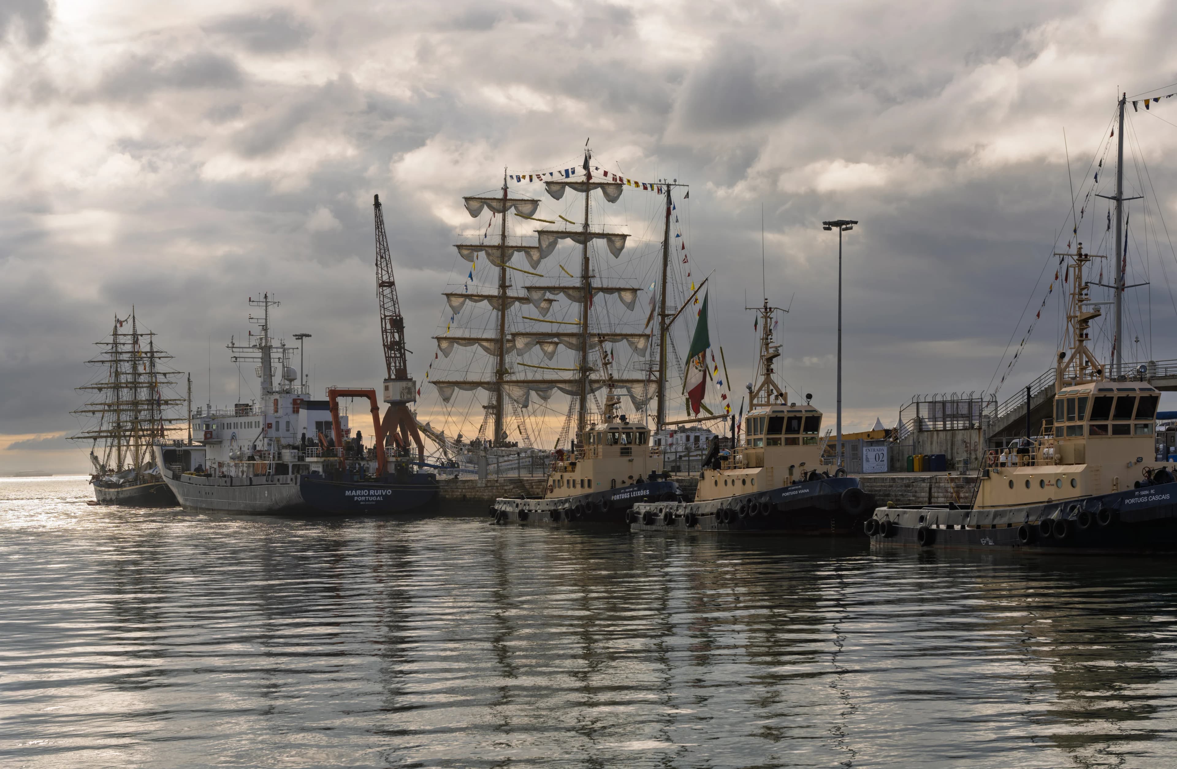 Small boats moored in calm water at sunrise in Lisbon, with a pale orange sky behind them.